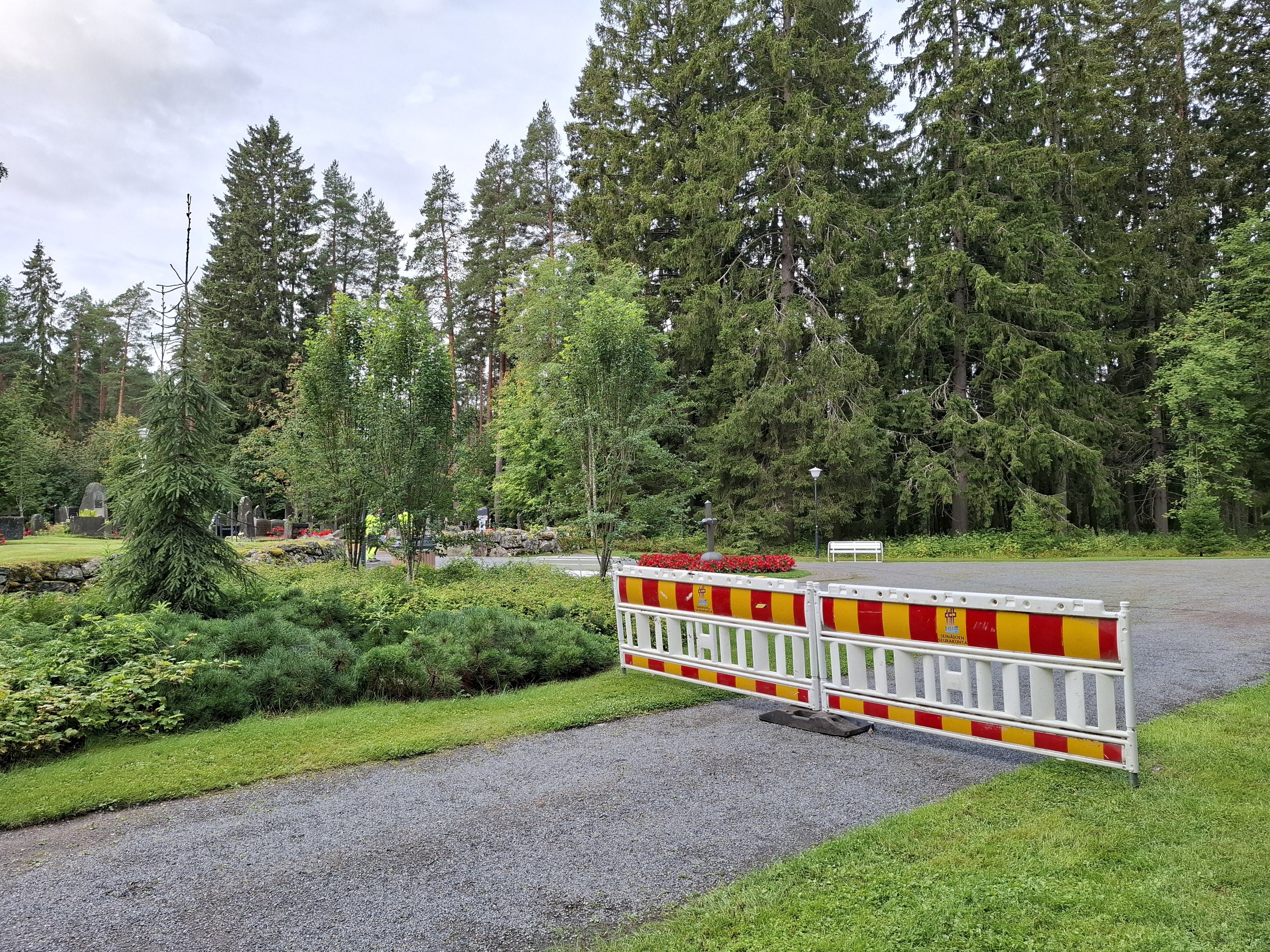 Kuvassa vehreää puistomaista aluetta, jonka tie on laitettu poikki puomeilla.