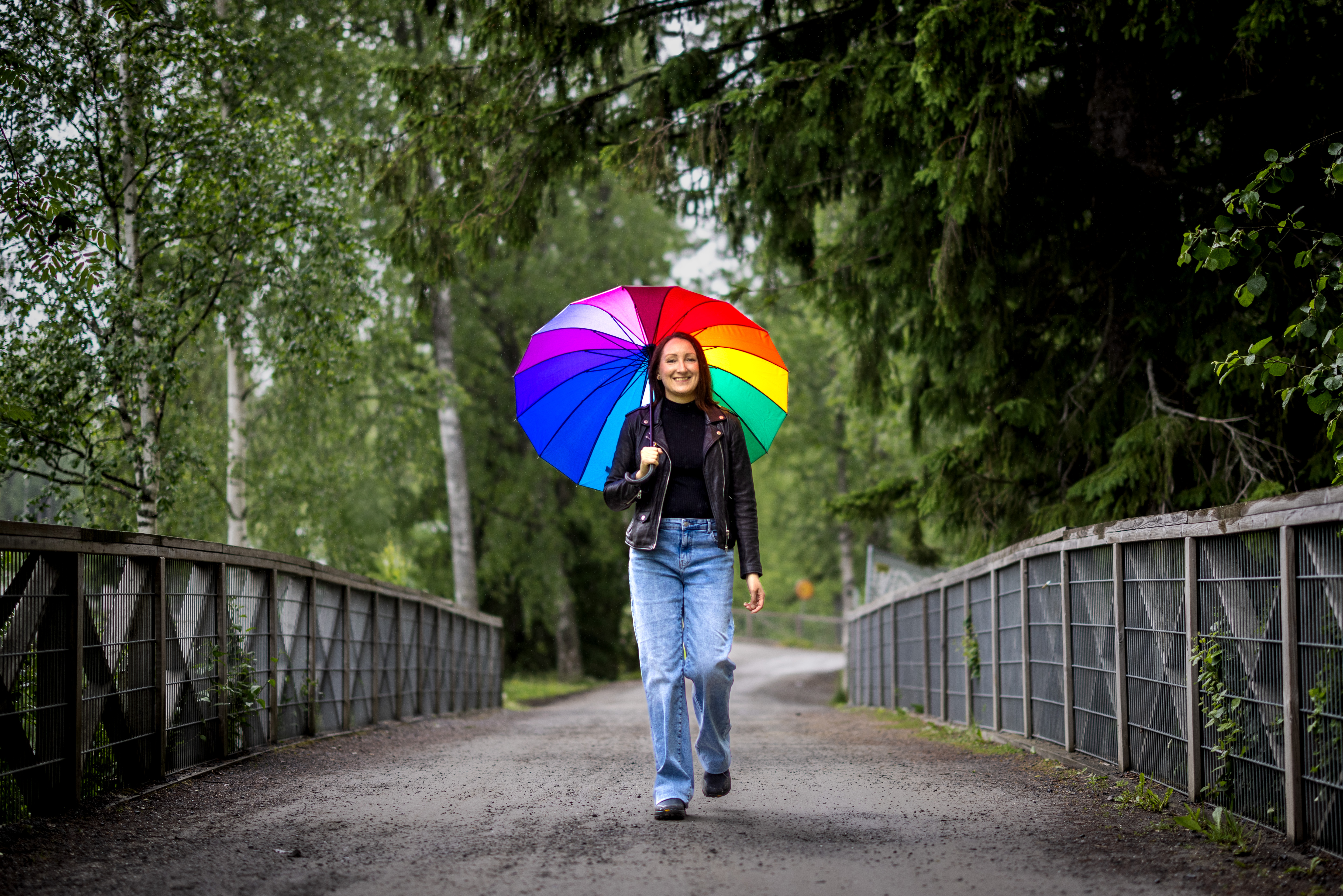 Henkilö kävelee sillalla sateenkaari sateenvarjo kädessään.