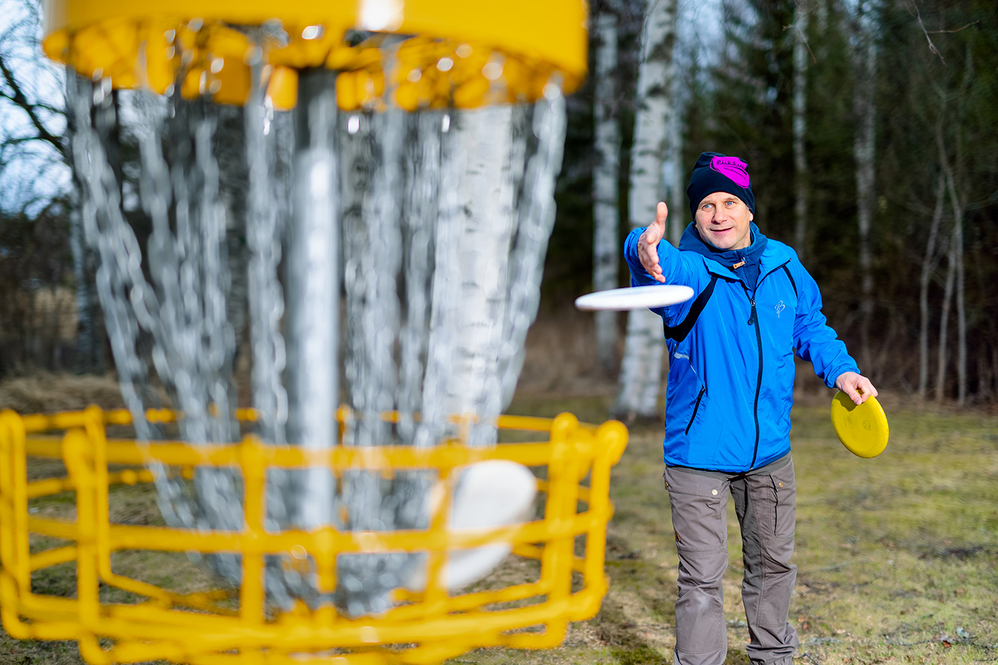 Mies heittää frisbeegolfia metsässä.