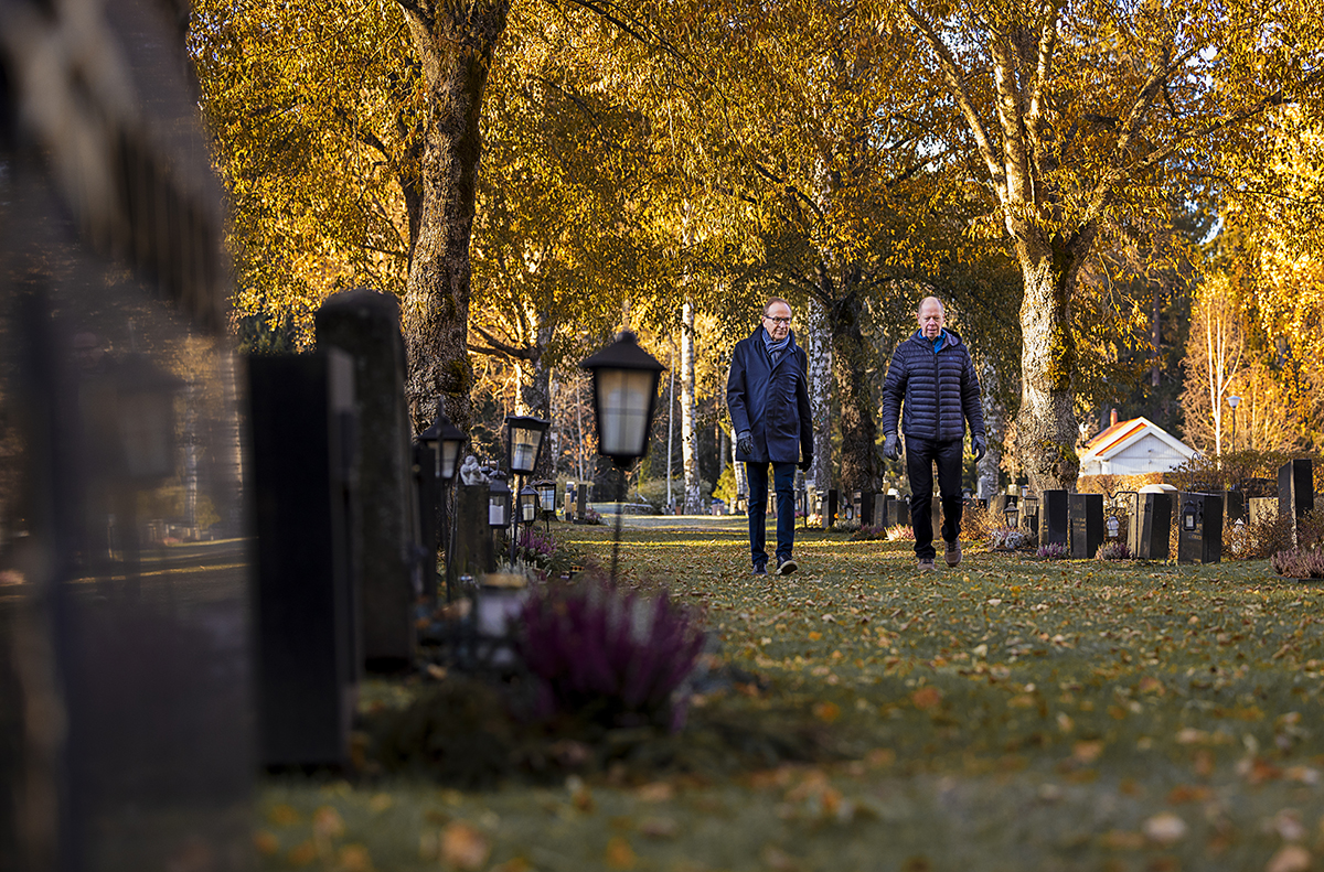Kaksi miestä kävelee syksyisellä hautausmaalla.