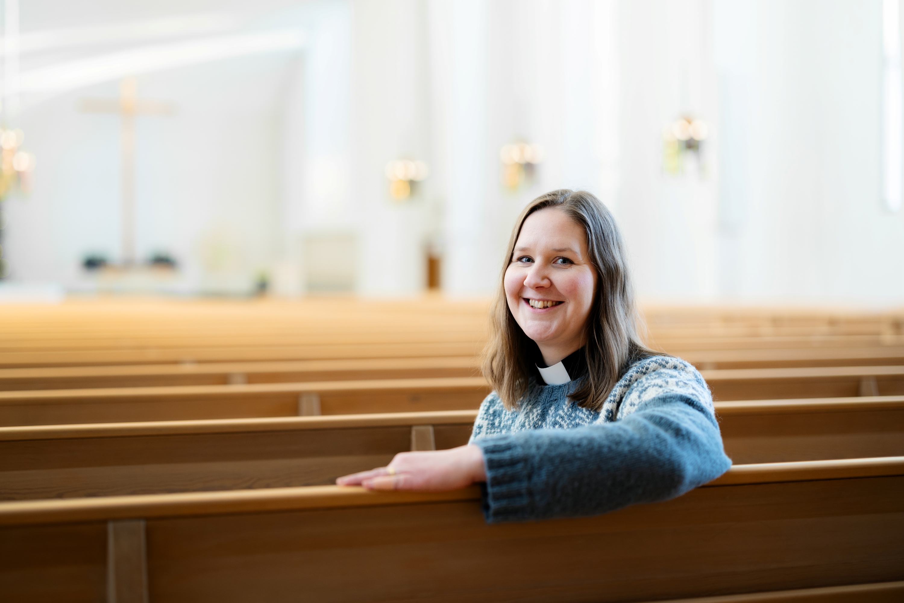 Rippikoulupastori Laura Launiala istuu kirkon penkissä ja kääntyy kohti kameraa. Taustalla alttarin risti.