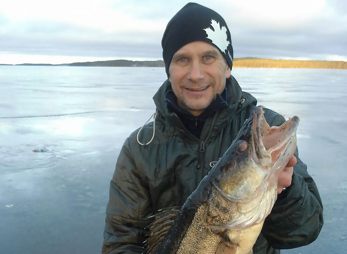 Markku Autio pitelee käsissään verkoilla saatua isoa kuhaa järven jäällä.