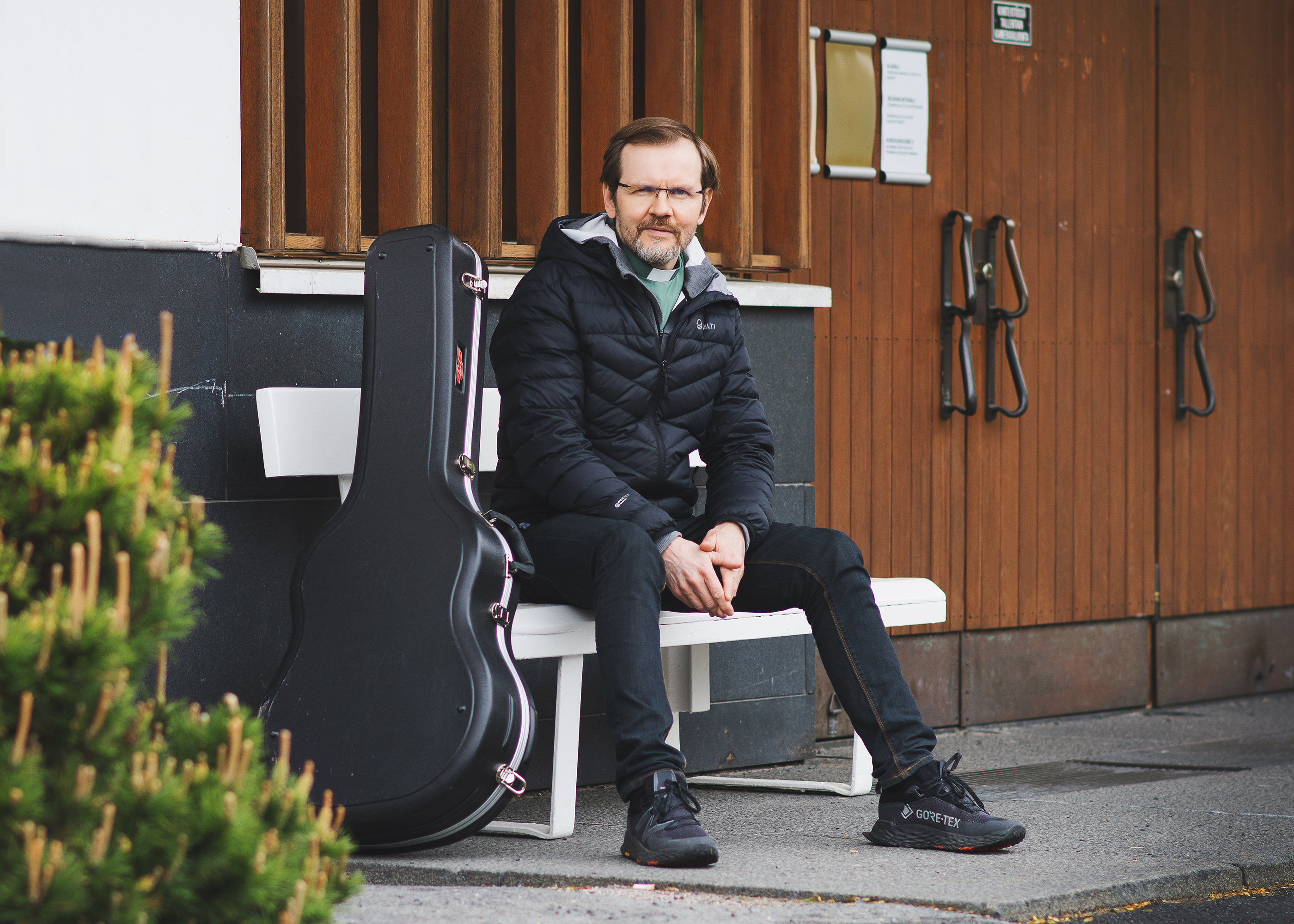 Diakoniajohtaja Otto Savolainen istuu penkillä. Vieressä kitarakotelo.