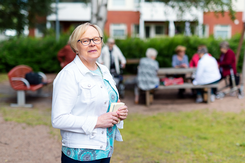 Kuvassa Aino Vähäsarja puistossa, taustalla naisten jutustelu- ja lauluhetkiryhmä.