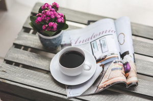 Kahvikuppi, kukkia ja aikakauslehti pöydällä.