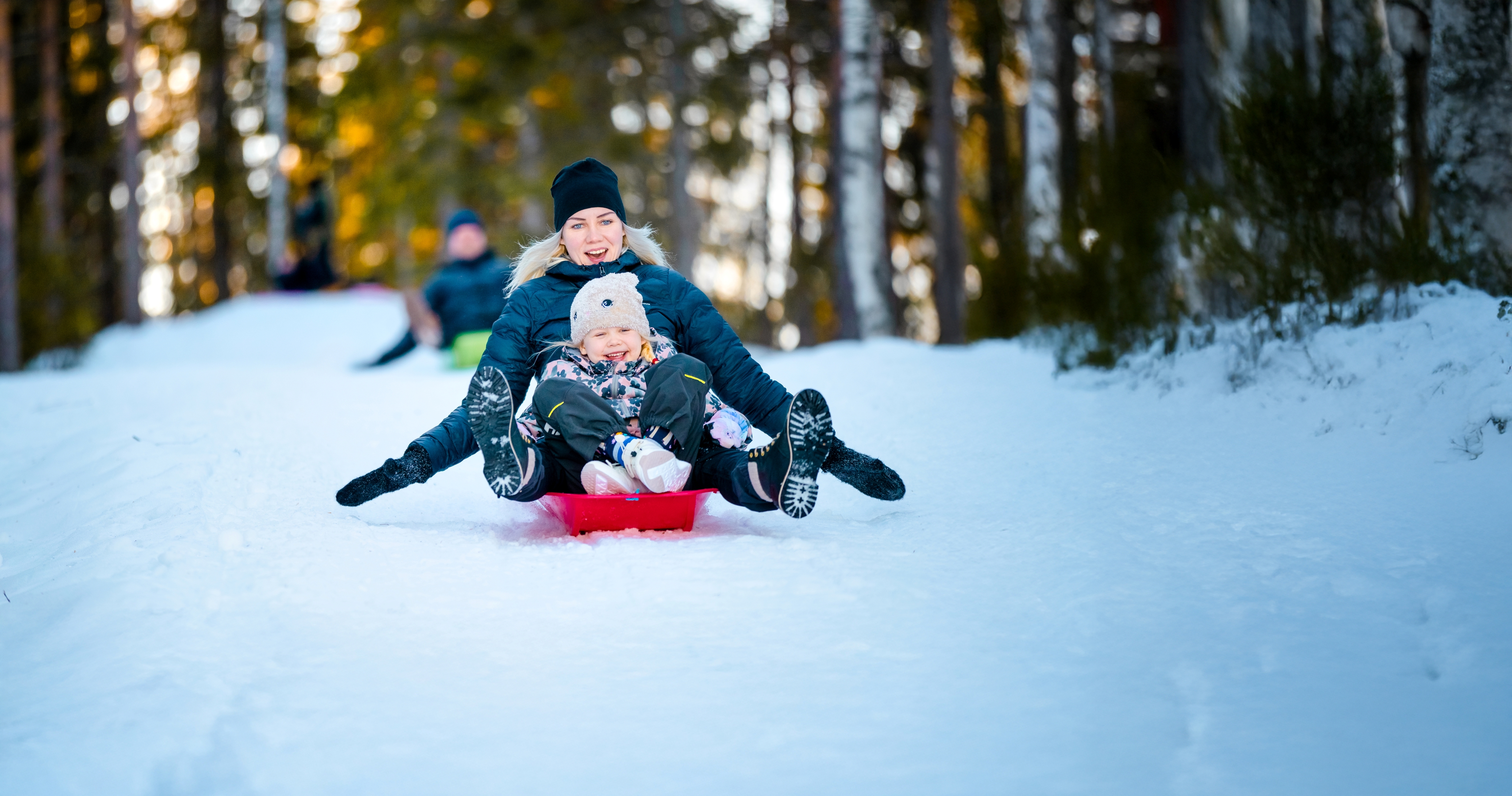 Nainen ja lapsi laskevat pulkalla mäkeä alas.