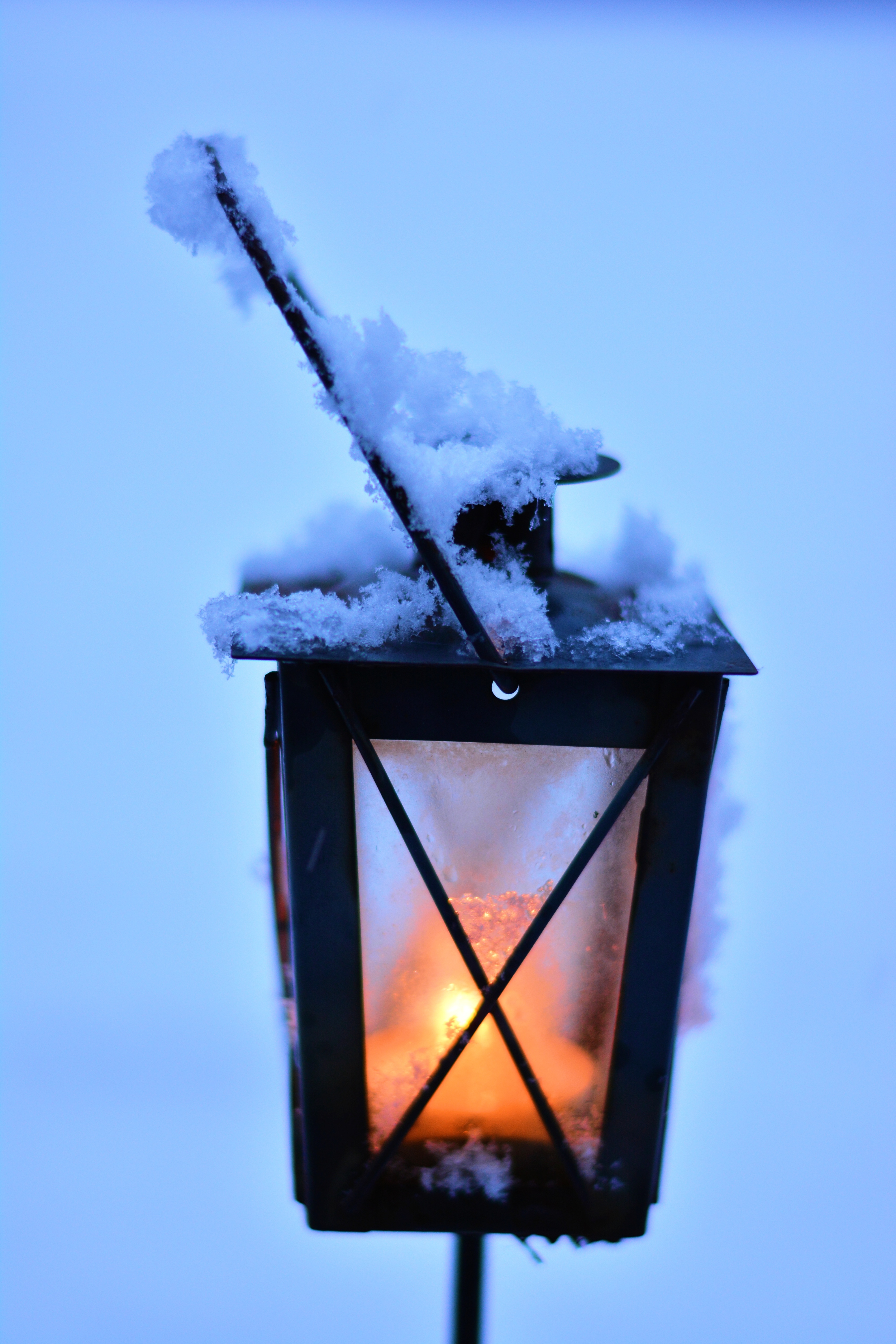 Hautalyhdyssä palaa kynttilä ja lyhdyn päälle on satanut lunta. On sininen hetki.