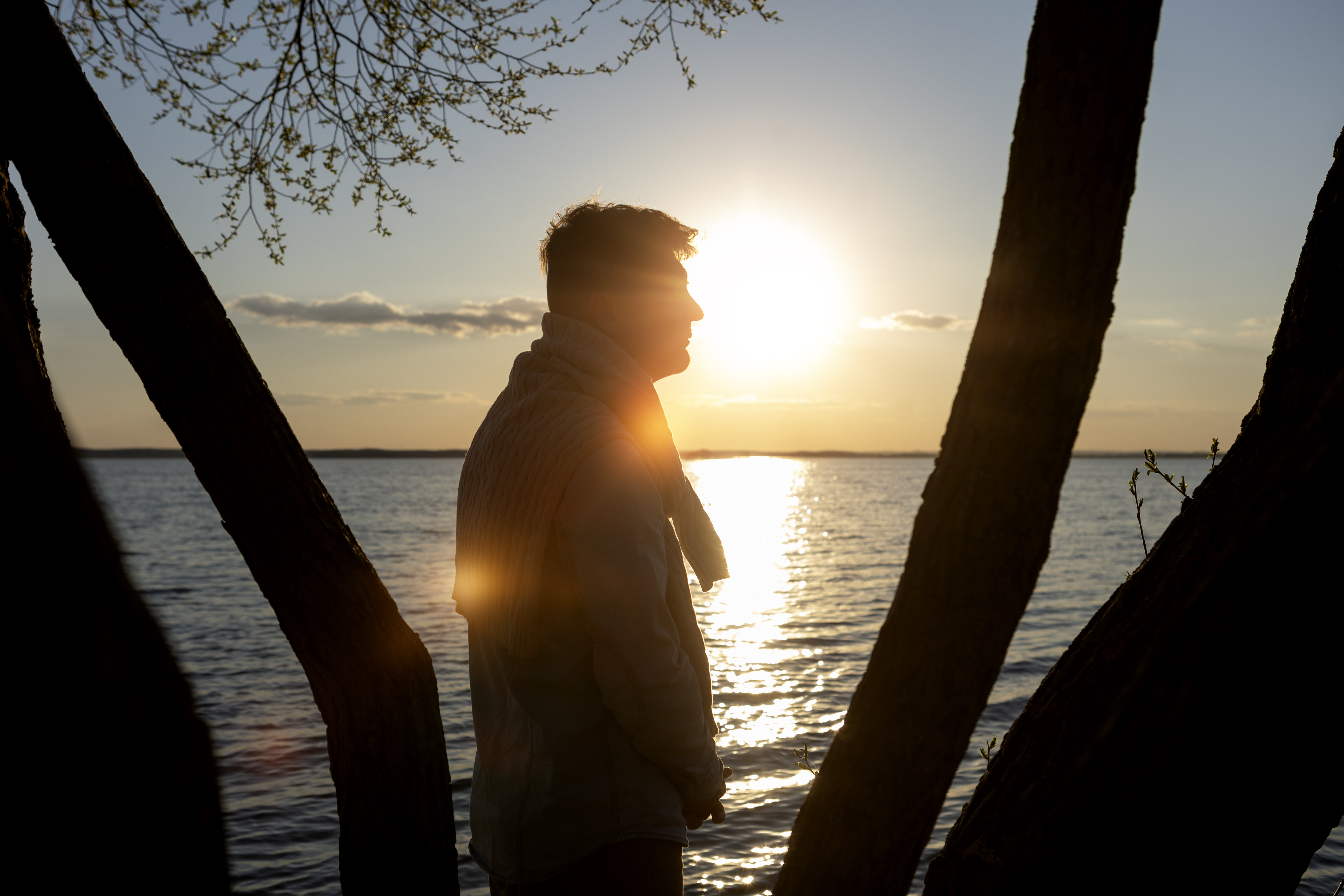 Miehen siluetti, taustalla auringonlasku ja järvimaisema.